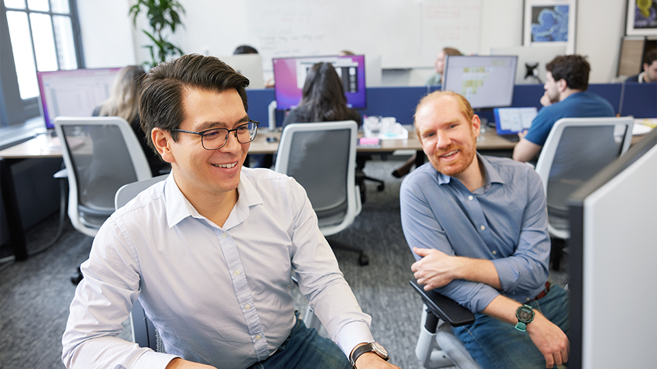 Coworkers smile while looking at work on a computer screen.